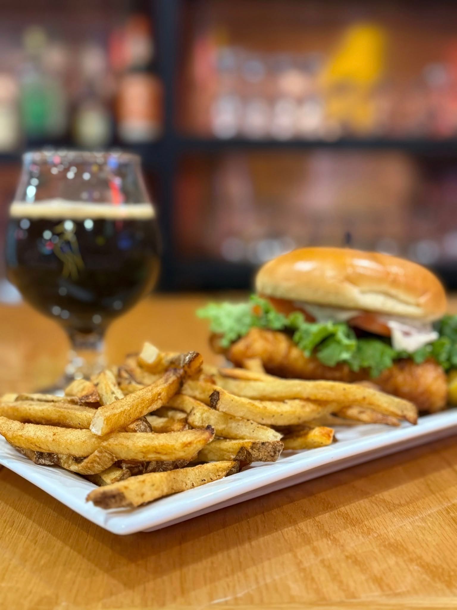 Crispy chicken sandwich with lettuce and house-cut fries alongside a dark beer