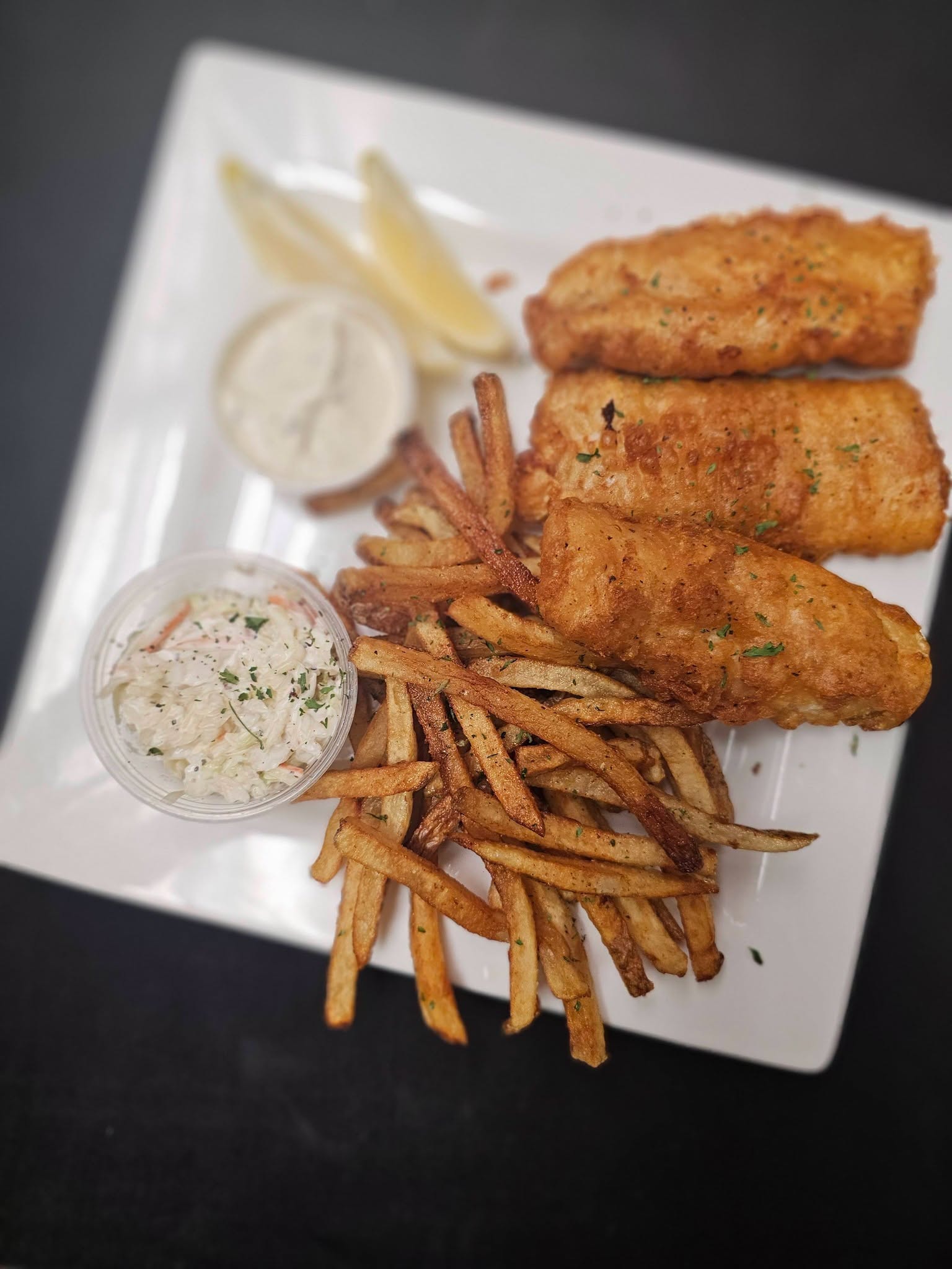 Beer-battered fish and chips with coleslaw, tartar sauce, and lemon